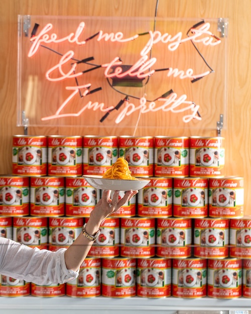 Delicious pasta dish in front of cans of San Marzano tomatoes and a neon sign that says "& tell me I'm pretty"